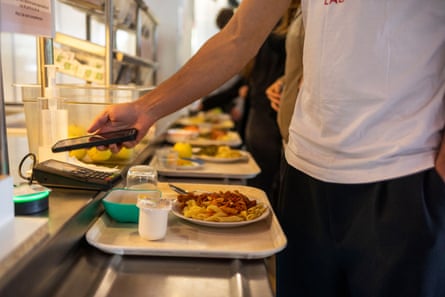Students push food-laden trays along a shelf in a cafeteria