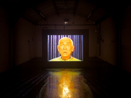 A dark room has a large screen at the end with a man's face showing on it