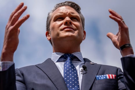 Defense Secretary Pete Hegseth raises both hands while speaking outdoors, looking upward