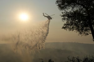 Water sprays out of a helicopter with burned smoky trees underneath