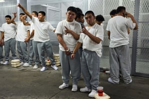 A group of men in white T-shirts and grey trousers handcuffed together in pairs make the ‘horns’ gesture with their free hands