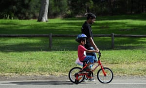 A young boy riding a bicycle is assisted by his dad in a park in Sydney
