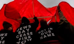 People under red fabric with shirts saying 'Jews say ceasefire now' and 'Not in our name'