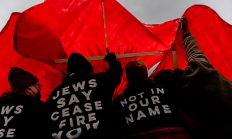 People under red fabric with shirts saying 'Jews say ceasefire now' and 'Not in our name'