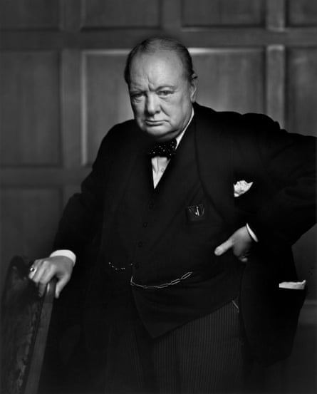 Winston Churchill wearing a dark suit and bow tie, holding a stick and looking stern, photographed in a wood-panelled room