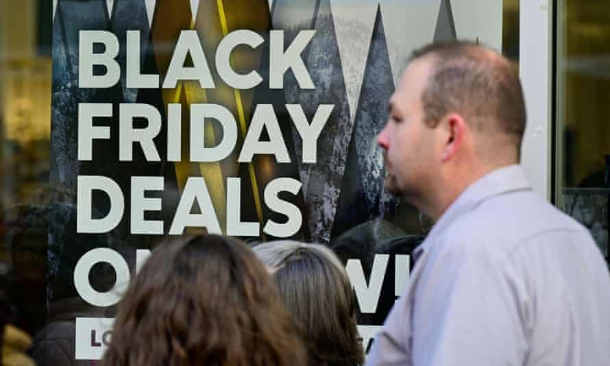 People standing in front of a Black Friday sale sign in a shop window.