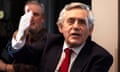 Gordon Brown, in a shirt, tie and suit jacket, smiles slightly as he raises his right hand while speaking