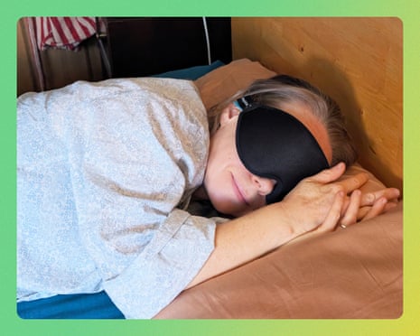 A person lies in bed wearing a black sleep mask and light-colored robe