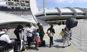 Asylum seekers walk outside Olympic Stadium as security guards look on in Montreal.
