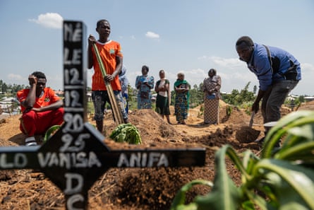 African men and women at the side of a rudimentary grave with wooden cross marker