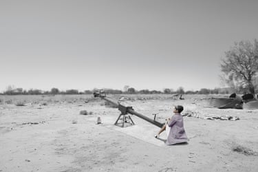 Mother (see saw) 2016. A mostly monochrome image of a desert. In colour, a woman in a light purple jacket sits on the lower end of a see-saw, looking at the sky.