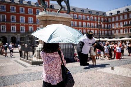 A woman in a town square in Madrid shelters from the sun under an umbrella