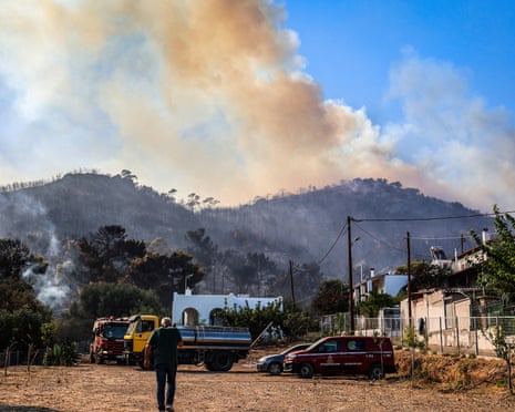 A man stands in front of a burnt area as smoke raises into the sky during a wildfire in the island of Salamis, near Athens, Greece.