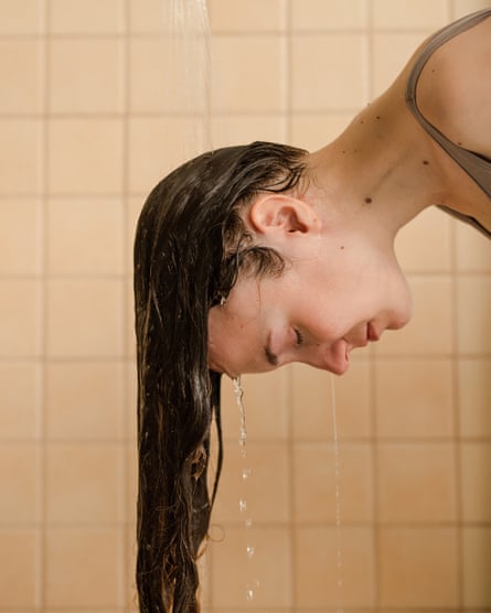 Jovem com a cabeça baixa lavando o cabelo no chuveiro