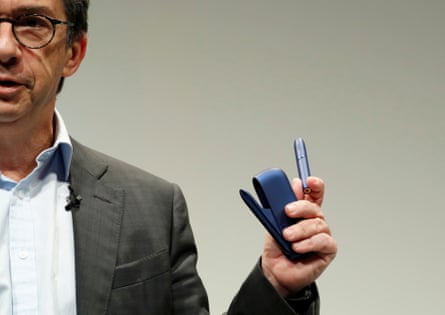 A middle-aged European man in a suit holds up a vape-like device 