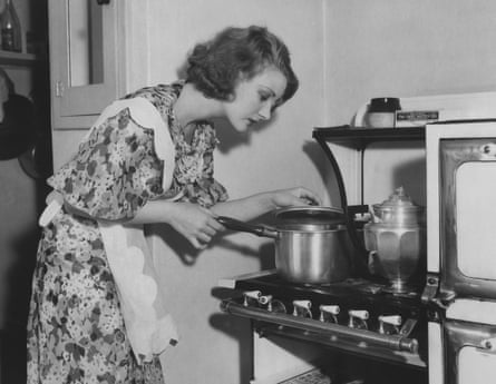 A 1950s housewife looking into a pot on a stove.