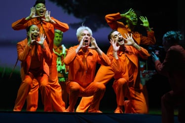 David Byrne performs on stage with backing singers; everyone is wearing orange outfits