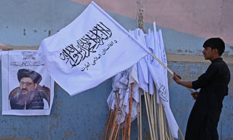 A vendor in Kabul holds a Taliban flag next to a poster of Taliban leader Mullah Abdul Ghani Baradar