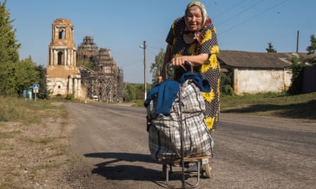An elderly woman pushes a shopping trolley stacked with belongings
