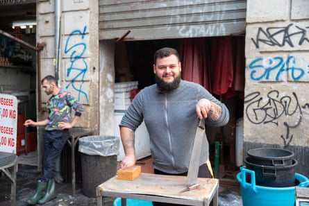 A man stands at a wooden table with a large knife