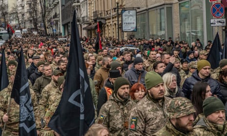 A large crowd of soldiers and civilians walks along a street