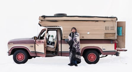 Juan, an immigrant from Mexico, with his Ford campervan in Santa Monica, California, US. He is standing outside the brown and cream campervan wrapped in a blanket
