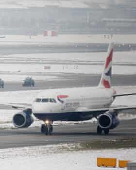 A team of snow ploughs are escorted between terminals as a British Airways plane taxis to Terminal 5 of Heathrow Airport in West London