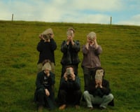 Six people on a grassy hillside hold rocks up to cover their faces. Folk band Trá Pháidín.