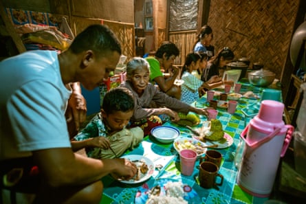 People sit eating a meal at a long table covered in a bright cloth