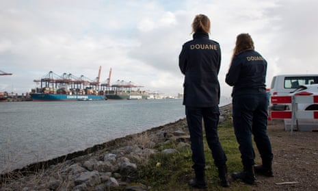 Two female police officers stand by the edge of the water looking at shipping activity in the distance.