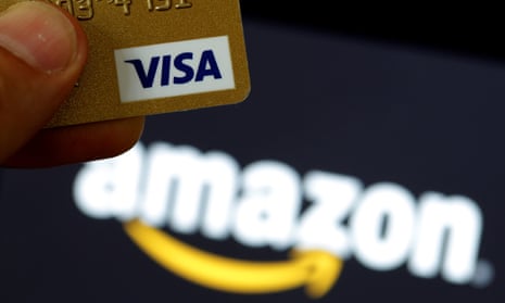 A visa credit card is held in front of an Amazon logo