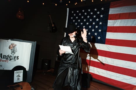 A man in a black cowboy hat reads on stage, an American flag in the background