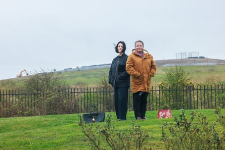 Donna Davidson and Dr Barbara Kneale standing outside on a lawn with the landfill site on a hill behind them