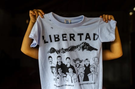 Some one hold up a T-shirt in front of their face with an illustration of 11 people under the word ‘libertad’.