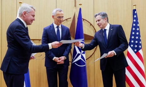 The Finnish foreign minister, Pekka Haavisto, left, hands over Finland’s accession document to the US secretary of state, Antony Blinken, right, as Jens Stoltenberg looks on.
