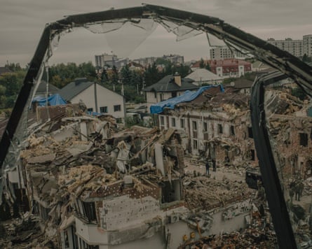 A residential building reduced to rubble seen through the twisted frame of a broken window