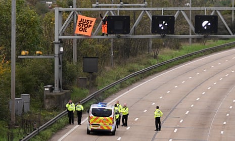 Police officers attempt to stop an activist as they put up a banner reading "Just Stop Oil" atop an electronic traffic sign along M25 on November 10, 2022 in London