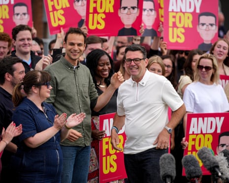 Andy Burnham stands beaming in front of a crowd holding 'Andy for us' placards