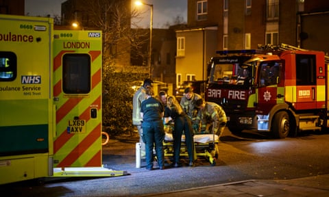 A London Ambulance Service crew respond to a 999 call in south London, where they find Clarice Freckleton, an unconcsious bed-bound woman who is being cared for in a hospital-issue bed at home, by her daughter Selina (who has five children of her own at the home) On this day, Clarice's 66 birthday, the LAS crew decide that she should be carried in to King's hospital but are unable to safely move her down from the fourth floor flat, so they call a local Fire Department crew to come and assist. Firemen from New Cross Fire Station come and bring Clarice downstairs and help the LAS crew get her into the ambulance. A day out with a London Ambulance Service (LAS) crew during their shift in south London. Laura Brown, 40 (brown hair) only joined the LAS in May and is a trainee paramedic. Jennifer Nelso, 24, is a fully qualified paramedic and has worked for the LAS for 18 months. London. Photograph by David Levene 30/11/22
