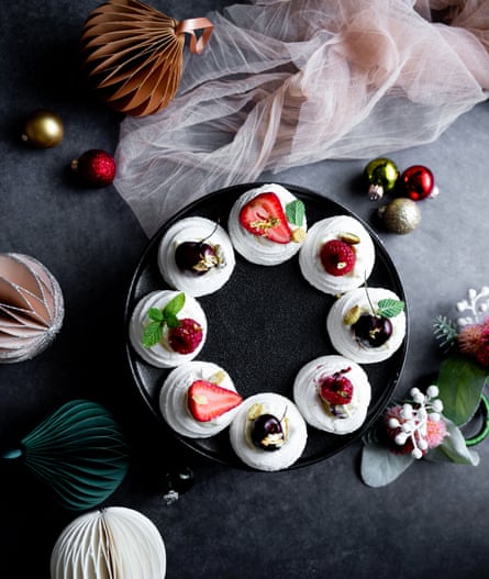 Individual meringue nests are arranged in a wreath pattern and decorated with strawberries, cherries, and raspberries.