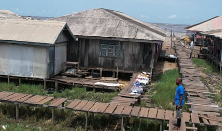 Emmanuel Aralu stands on a stilted wooden boardwalk that runs around houses near the sea.