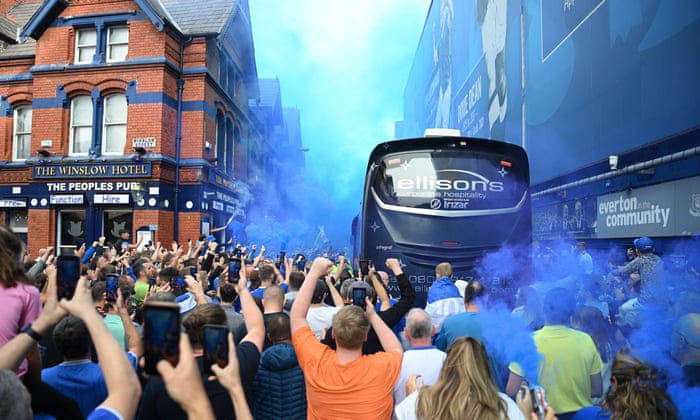 People, fresh out of the pub, salute the arrival of their team on their bus to their club.