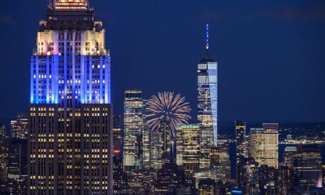 Fireworks explode behind landmark buildings of the Manhattan city skyline including the Empire State building and One World Trade Center, illuminated in blue and gold