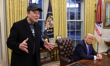 a man in a black Maga hat speaks next to man in a suit seated at a desk