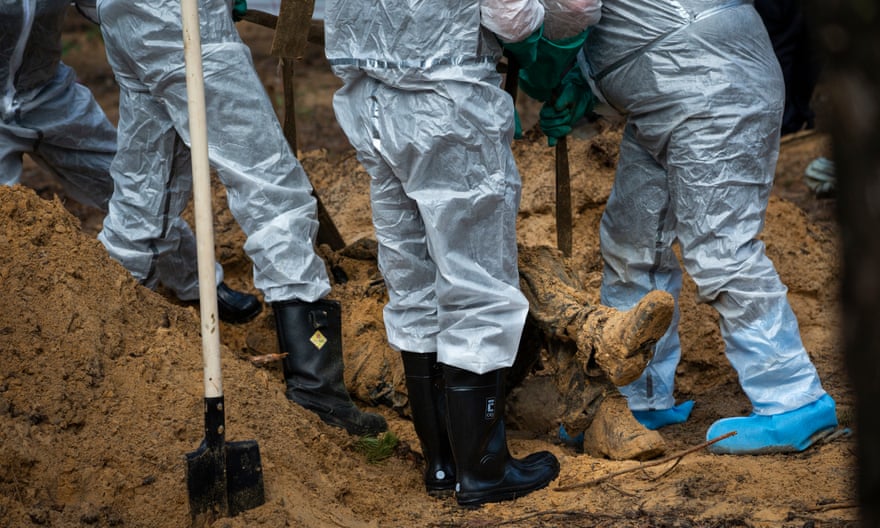 Members of the emergency services in protective gear dig up a body at the mass burial site in Izium