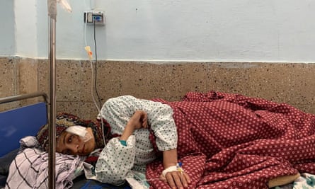 An injured Afghan woman lying on her side in a basic hospital bed.