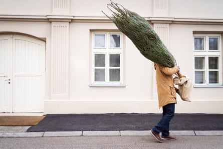 Unrecognizable man carrying Christmas tree while walking down a street.