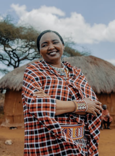 A Maasai African woman in traditional checked cloak and dress by a thatched hut