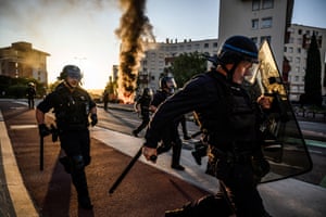 Police officers with helmets and shields move away from a fire in a street
