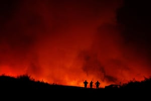People stand in silhouette against a red backdrop of wildfires
